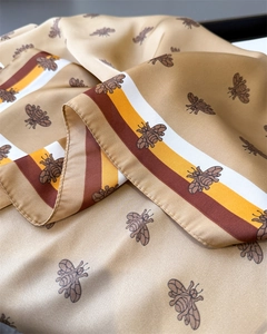 Detailed macro shot of silky gold scarf fabric featuring honeybee prints and striped edges