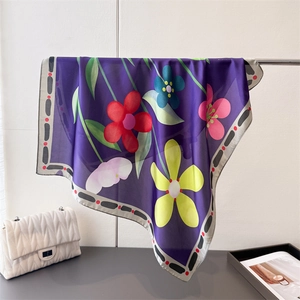 Détail d'un foulard en soie à imprimé floral drapé à côté d'un sac blanc matelassé