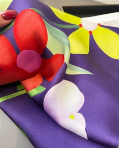 Détail d'un foulard en satin de soie aux fleurs rouges et jaunes sur un tissu violet foncé