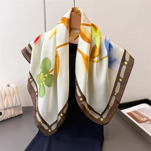 Détail d'un foulard en soie à fleurs vertes et bordure marron suspendu à un cintre décor