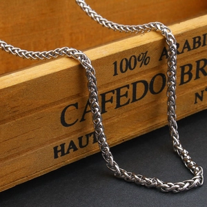 Collier chaîne tressée en acier inoxydable poli présenté sur une boîte en bois rétro