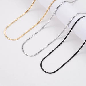 Chaînes gourmettes plates en or, argent et noir suspendues sur un support blanc