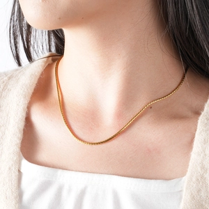 Élégante chaîne en épi d'or en acier inoxydable portée par un mannequin sur un pull beige