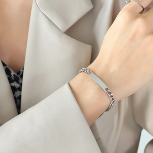 Close-up of a silver Cuban chain ID bracelet with a blank rectangular polished metal plate