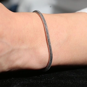 Makroaufnahme eines polierten Schlangenknochen-Armbands aus Edelstahl am Handgelenk