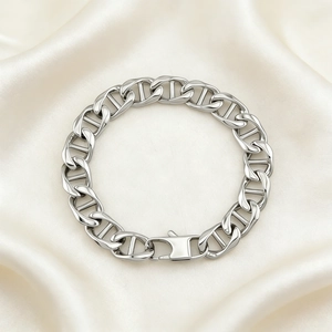 Detailed close-up of polished stainless steel anchor link bracelet on cream silk fabric