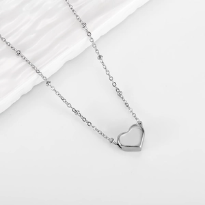 Polished silver heart pendant necklace with beaded fine chain on white textured surface