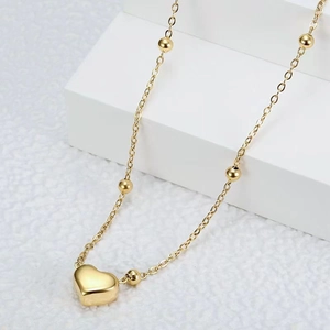 Detailed close-up of 18k gold heart pendant and round beads on a slim minimalist chain