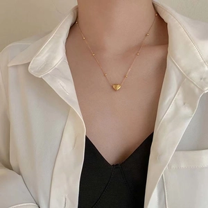 Detail of 18k gold heart pendant necklace with beaded chain on model's neck