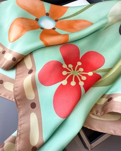 Vue macro détaillée d'un foulard en soie vert menthe avec des imprimés floraux orange vifs