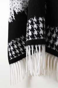 Detail of classic houndstooth knit scarf featuring white long fringes and soft texture