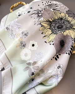 Detail of silk scarf showing yellow sunflower print and smooth satin texture on gray surface
