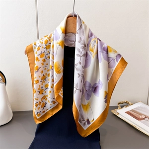Elegant white silk scarf with purple floral print and gold borders on a wooden hanger