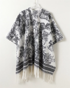 Detail showing the abstract ink wash texture and fringe tassels on the knit poncho