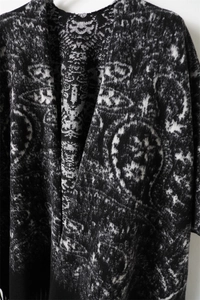 Detail of black and white geometric jacquard knit shawl with soft fleece texture and fringe