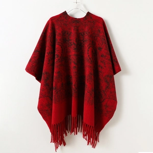 Close-up detail of retro jacquard pattern and long fringe on red knit poncho shawl