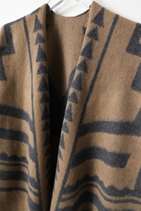 Dettaglio dei motivi geometrici e della texture morbida sul poncho in maglia marrone