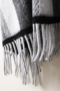 Detailed close-up of grey and white plaid scarf with soft cashmere-like texture and long tassels