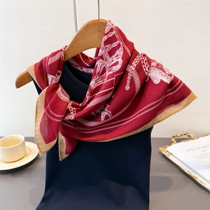 Detail of red equestrian silk scarf featuring white carriage patterns and khaki border