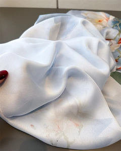 Gros plan sur le tissu léger de l'écharpe en soie bleu clair aux motifs floraux blancs