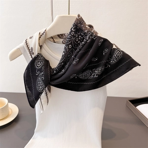 Detail of paisley pattern black and white silk scarf tied on a white knit vest top