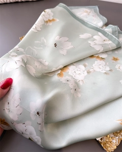 Detailed close-up of light green silk scarf with delicate floral prints and rolled edges