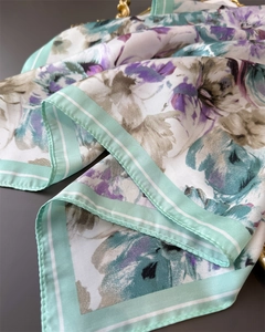 Detail of elegant floral silk scarf with green striped border on a matte grey surface