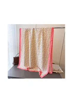 Detailed view of the pink border and geometric H letter monogram on the light silk scarf