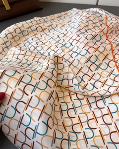 Detailed macro view of geometric U-pattern silk scarf with vibrant orange edge stitching