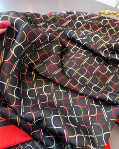 Macro detail of geometric satin scarf showing silk texture and red hemmed edges