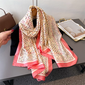 Silk-like geometric long scarf in pink and beige, draped elegantly on a stylish table