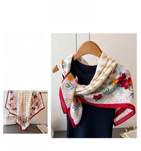 Dettaglio macro di un foulard in seta floreale con bordi rossi e motivo monogramma