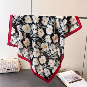 Detailstruktur des schwarzen Seidenschals mit Blumenmuster und rotem Rand am Display