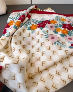 Dettaglio di un foulard in seta con stampa floreale e motivo monogramma su piano grigio