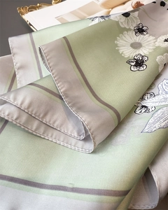 Close-up of elegant white daisy floral print on soft light green silk square scarf