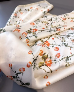 Détail du motif floral orange sur foulard en soie synthétique crème avec bord roulé