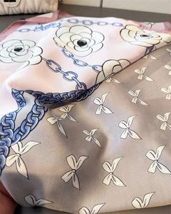 Detailed close-up of silk scarf featuring camellia, chain, and bow patterns in soft pink