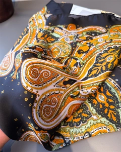Macro detail of silk-like paisley scarf fabric showing vibrant orange and green patterns