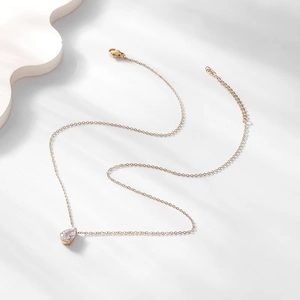 Minimalist gold teardrop necklace with zircon pendant on white geometric display