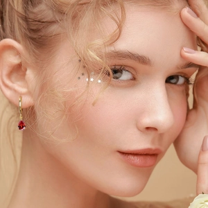 Close-up of elegant gold hoop earrings with red teardrop zircon pendants on a model