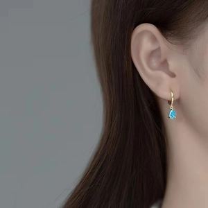Close-up of teardrop blue zircon earring on model with elegant golden finish detail