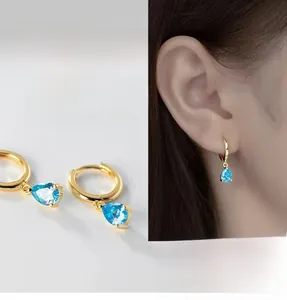 Detail view of golden teardrop earrings with blue zircon on model showing elegant design