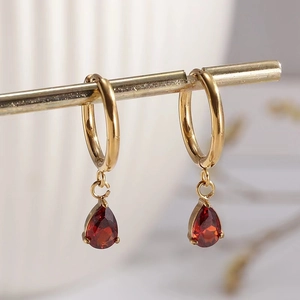 Elegant gold hoop earrings featuring a pear-cut red zircon drop on a metallic display stand