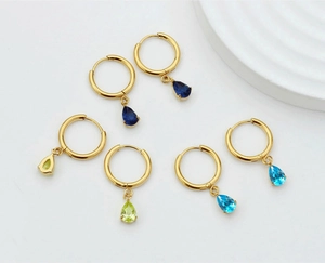 Detailed shot of teardrop zircon earrings in blue and green on golden steel hoops
