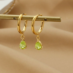 Detail of gold teardrop earrings with green zircon on a satin background