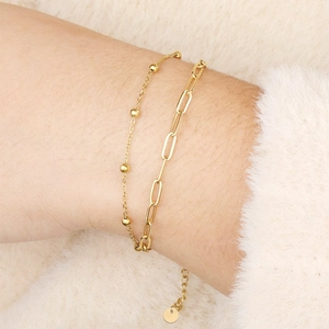 Bracelet élégant à double chaîne dorée avec trombone et perles porté au poignet