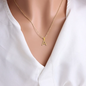 Primer plano de collar con colgante de letra A dorada con perlas usado por una modelo