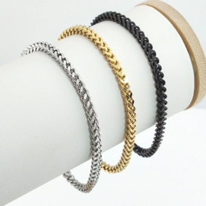 Detailed view of wheat chain bracelets in gold, silver, and black polished finishes