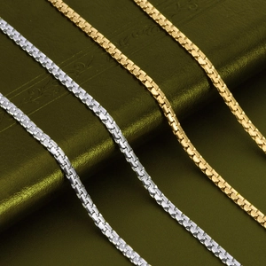 Macro shot of silver and gold stainless steel box chain necklaces on leather background