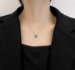 Close-up of minimalist stainless steel U-shaped turquoise pendant on a model in a black suit